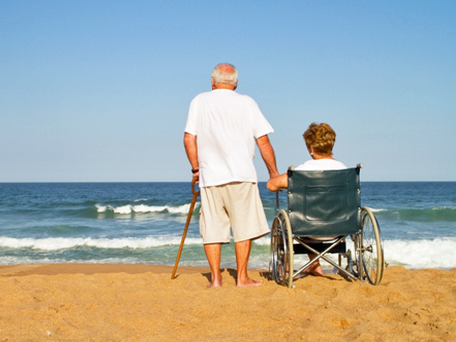 Man with cane and woman in wheelchair on beach